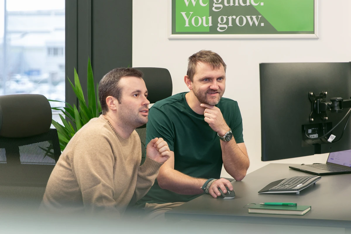 Zwei Personen sitzen nebeneinander an einem Schreibtisch und schauen gemeinsam auf einen Bildschirm.