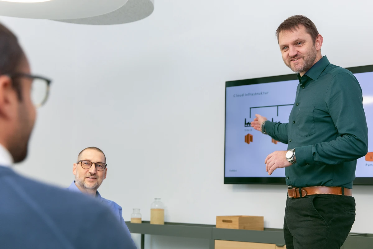 Cloud-Architektur und skalierbare IT-Infrastrukturen von kubidat. Eine Person steht vor einem Bildschirm und erklärt eine Grafik während einer Besprechung.