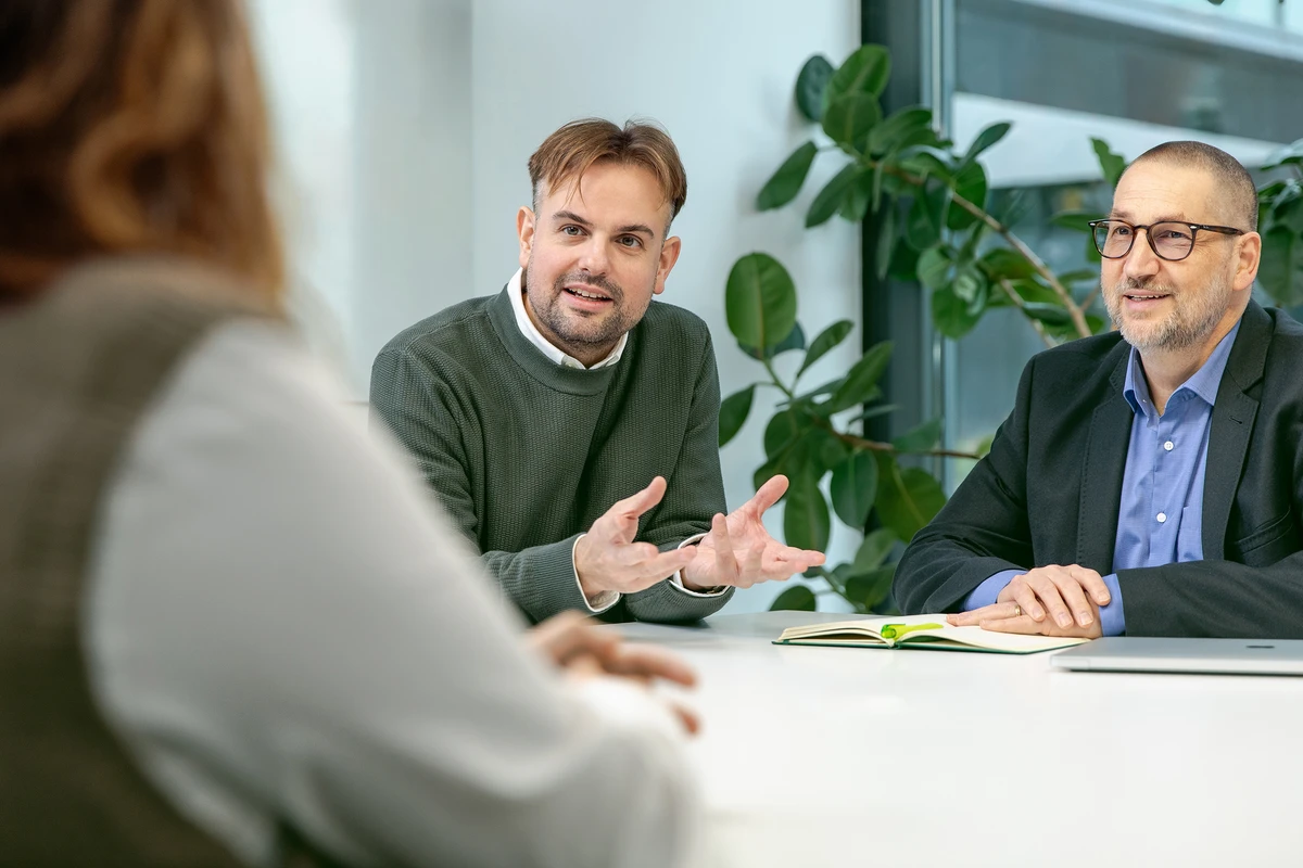 kubidat berät Kunden zu Data Consulting und individuellen IT-Lösungen. Zwei Personen sitzen an einem Tisch und sprechen mit einer weiteren Person im Vordergrund.