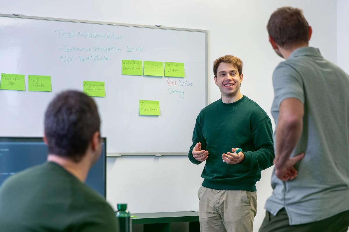 kubidat Team plant CI/CD, DevOps und moderne Dateninfrastrukturen. Zwei Personen stehen und eine Perso sitzt vor einem Whiteboard und besprechen Post-Its.