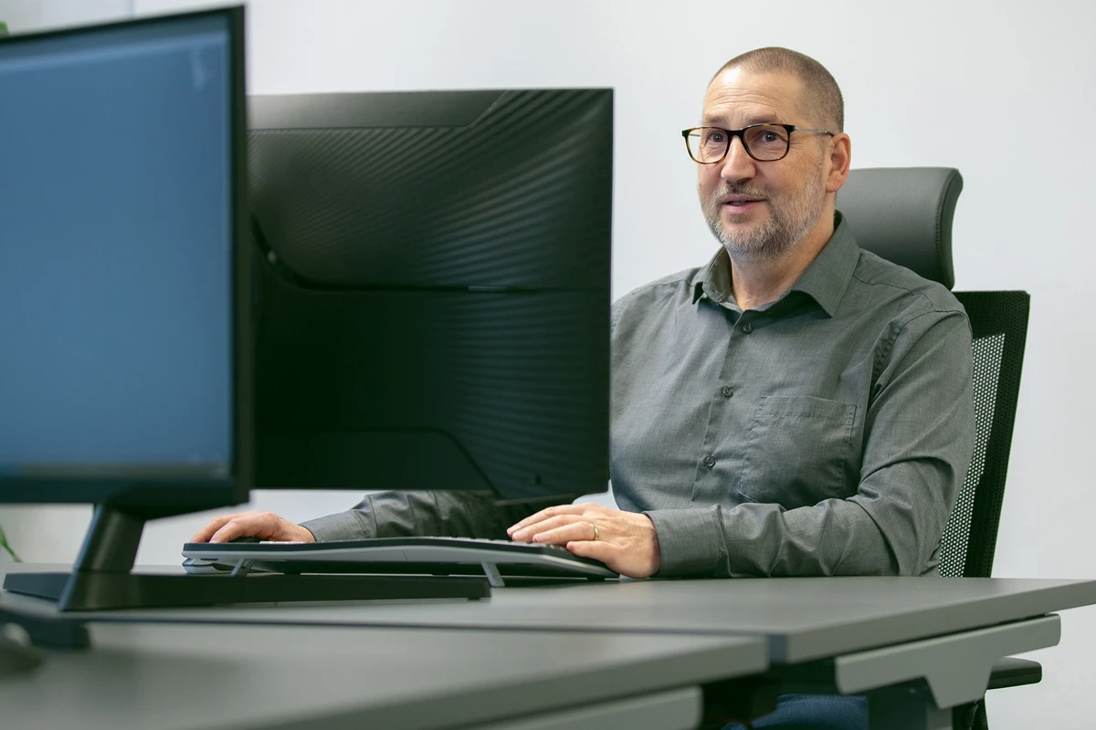 Softwareentwicklung und IT-Beratung bei kubidat. Person sitzt an einem Schreibtisch vor einem großen Monitor und arbeitet am Computer.
