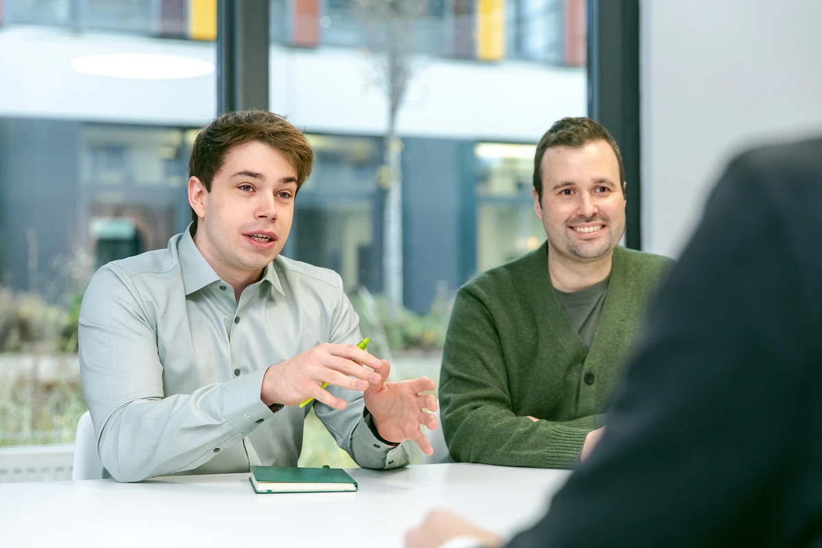 Ganzheitliches Data Consulting für komplexe IT-Projekte. Zwei Personen sitzen nebeneinander in einem Meeting und sprechen mit der Person im Vordergrund.