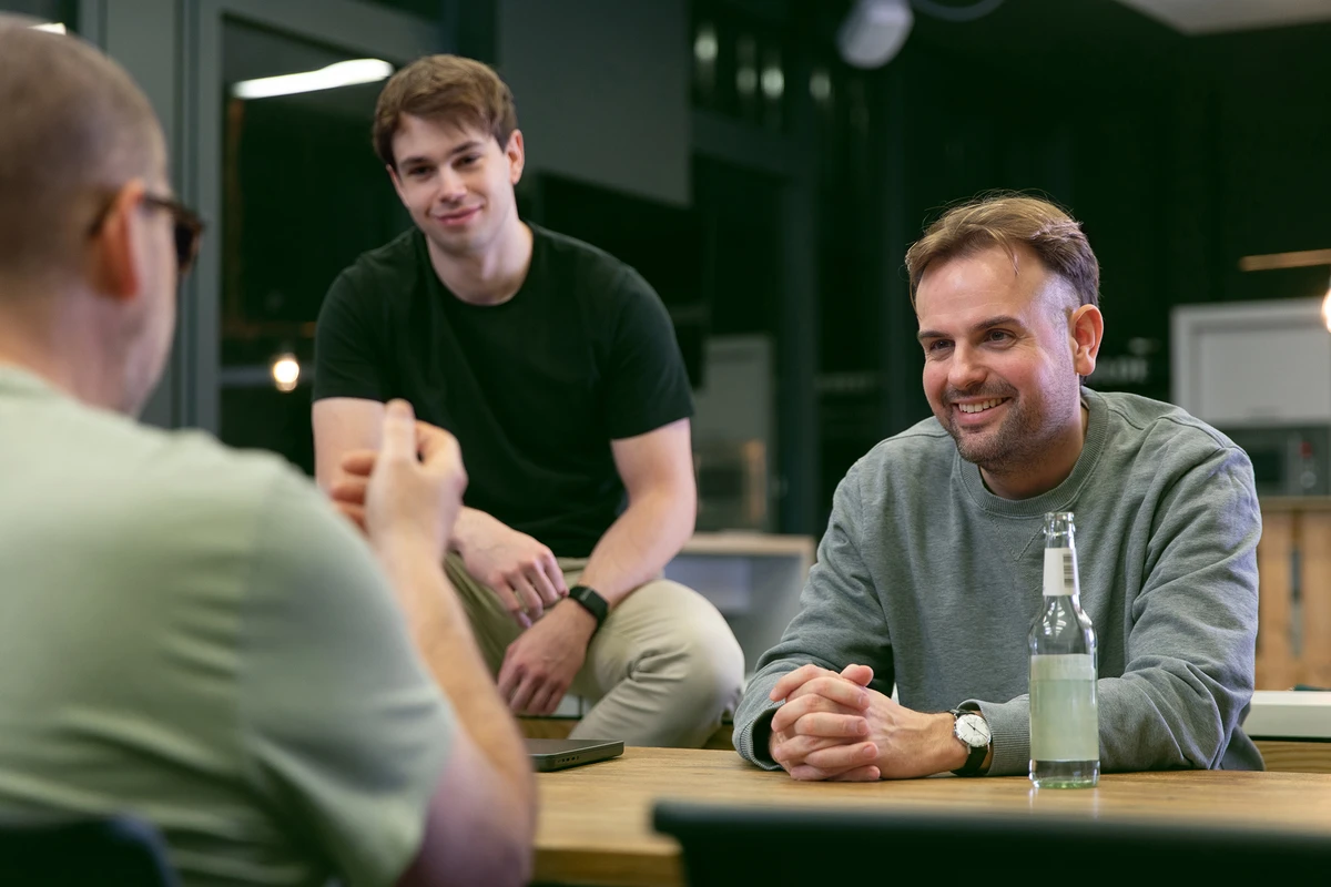 Moderne Arbeitswelt im Bereich Data Consulting bei kubidat. Lockere Atmosphäre in der Küche, drei Personen führen ein Gespräch.